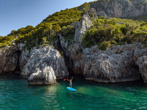 Young woman paddle boarding by rocky seaside. drone shoot.