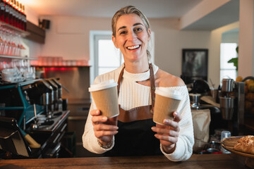 Blonde waitress holds a fresh to go coffee as the cafe owner prepares drinks behind the counter creating a lively business scene