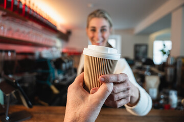 Blonde waitress presents a to go coffee while the cafe owner prepares drinks behind the counter reflecting teamwork and service