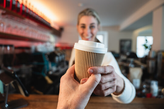 Blonde waitress presents a to go coffee while the cafe owner prepares drinks behind the counter reflecting teamwork and service