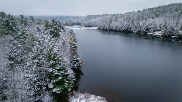 Aerial view of dark waters reflecting the overcast sky, contrasted by snow-laden trees in the White Mountains, New Hampshire, USA.