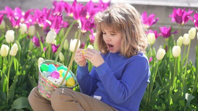 Easter child in blossom spring park. Kid hunting Easter eggs near tulips. Kid play wit Ester eggs outdoor. Kids portrait in garden. Dreamy and surprised child look. Kid play with Easter eggs.