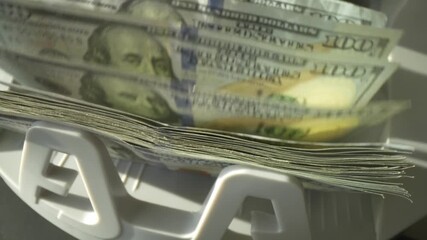Closeup currency counting machine counting dollar. Slow motion of cash counting machine counts 100 dollar bills USD banknotes. Cash bill counter money machine. Finance banking credit deposit cash. - Powered by Adobe