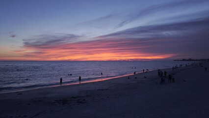 Aerial view of fiery sunset paints the sky in vivid hues over the tranquil beach waters, silhouettes of people enjoying the serene evening, Treasure Island, Florida, United States.