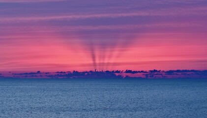 Aerial view of crepuscular rays pierce through the horizon, casting an ethereal glow over the tranquil sea, painting the sky in hues of pink and purple, Treasure Island, Florida, United States.
