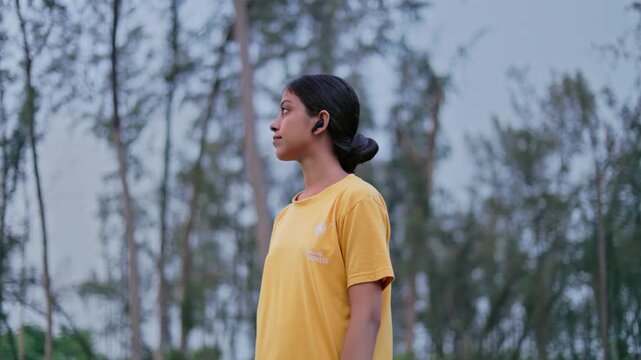 Female adventurer standing alone in a forest wearing earpods and looking at the scenic view, exploring nature and enjoying peaceful landscape view.