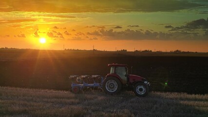 Aerial view of tractor with agricultural machinery cultivates the arable land at sunset and prepares the soil for sowing crops. Drone footage of a tractor plowing the land, beautiful rural landscape