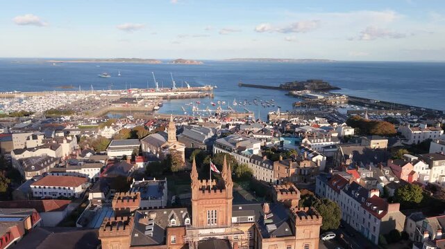View from Elizabeth College across St James and rooftops of St Peter Port Guernsey towards harbour Herm Sark and Jethou in the distance in bright afternoon sunshine on calm day