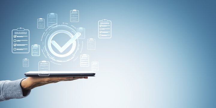 Hand holding tablet with digital checkmark and checklist icons on abstract light blue background representing approval and digital documentation.