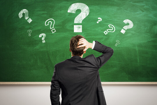 Confused man in suit standing before green chalkboard with floating question marks symbolizing curiosity, problem-solving, and education concept.