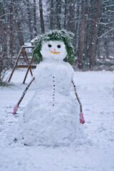 Cheerful snowman in a snowy garden with fir branches and gloves.