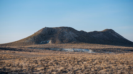 barren landscape with dry grass and rocky hills under clear blue sky, rugged terrain with visible erosion and sparse vegetation, remote and arid environment, vast natural scenery