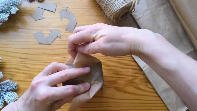 Gift wrapping made from eco-friendly materials against a background of a recycling symbol and Christmas tree branches. Fold the edges of the packaging
