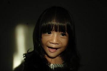 Portrait of a young girl standing in low-key lighting with a beam of natural light illuminating part of her face. She looks to the side with a calm expression, creating a cinematic