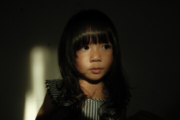 Expressive portrait of a smiling young girl in dramatic shadow lighting. The focused beam of light highlights her joyful expression, creating a warm and cinematic feel with strong contrast.