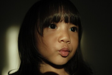Close-up portrait of a girl making a cute pout expression under dramatic artistic lighting. Shadows and highlights create a cinematic and emotional atmosphere.