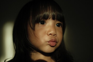 Close-up portrait of a girl making a cute pout expression under dramatic artistic lighting. Shadows and highlights create a cinematic and emotional atmosphere.