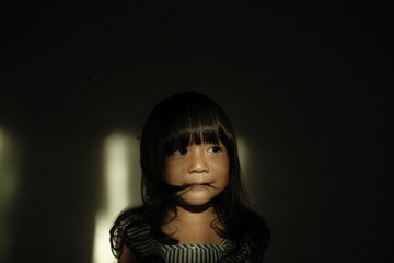 Portrait of a young girl with windblown hair illuminated by a dramatic beam of sunlight. Soft shadows emphasize her thoughtful expression in a cinematic indoor setting.