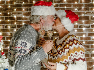 Happy senior couple exchanging a kiss celebrating together the Christmas season toasting with white wine and enjoying a festive night against a backdrop of warm decorative lights