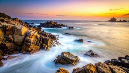 A dramatic sunset paints the sky with vibrant colors over a rugged coastline where waves crash against large rocks.