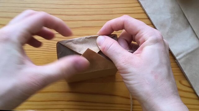 Gift wrapping made from eco-friendly materials against a background of a recycling symbol and Christmas tree branches. Bend the edges of the wrapping with your fingernails.