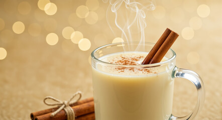Hot Christmas eggnog in a glass mug with cinnamon sticks. Traditional festive winter drink with steam on a cozy holiday background with golden bokeh