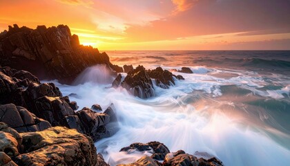 A dramatic sunset illuminates a rugged coastline where powerful waves crash against dark, jagged rocks, creating a misty spray.