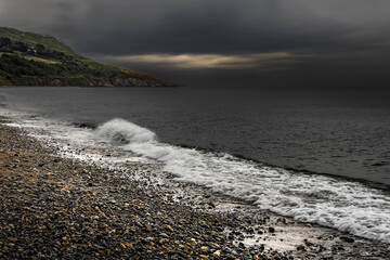 Dramatic seascape showing breaking wave and dark clouds over rugged irish shoreline