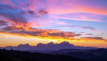 A breathtaking sunset paints the sky with fiery orange and soft purple hues, casting dramatic shadows over a jagged mountain silhouette and rolling hills below.