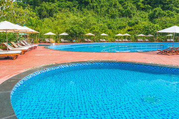 A swimming pool with several sun loungers in a luxurious tropical resort on a sunny day