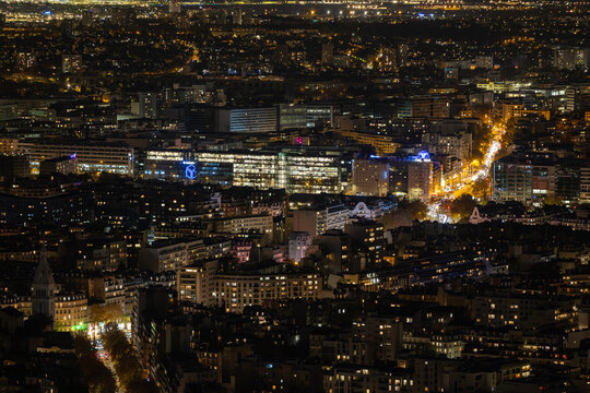 Aerial view of the vibrant cityscape glows with warm light, illuminating the buildings and streets in a mesmerizing display of urban life, Paris, Ile-de-France, France.