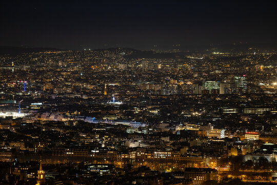 Aerial view of a glittering cityscape unfolds under the cloak of night, lights painting a vibrant tapestry across the horizon, Paris, Ile-de-France, France.