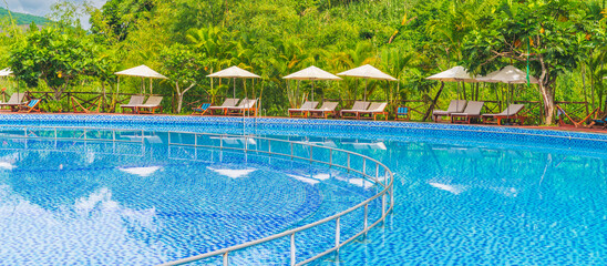 A pool with clear water surrounded by palm trees and sun beds on a sunny day