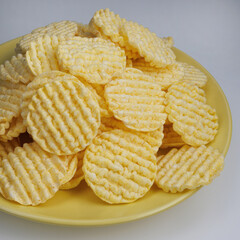A pile of corn chips on a yellow plate. Round corn chips. Ribbed chips.