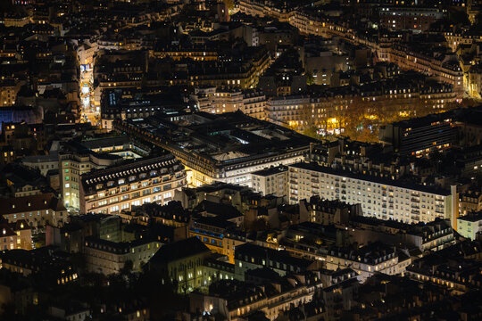 Aerial view of the vibrant city lights illuminating the architectural tapestry, casting a warm glow over buildings, Paris, Ile-de-France, France.