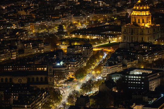 Aerial view of the illuminated D&ocirc;me des Invalides glows amidst the dark cityscape, casting a warm light over the Parisian night, Paris, Ile-de-France, France.