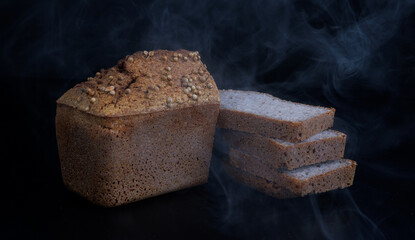 Half a loaf and pieces of sliced buckwheat bread on a black background. Steaming bread.