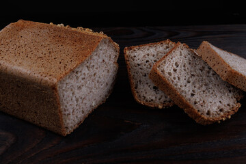 Half a loaf and pieces of sliced buckwheat bread on a dark wooden background.
