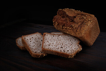 Half a loaf and pieces of sliced buckwheat bread on a dark wooden background.