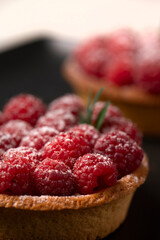 two raspberry tart on a black plate .