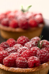two raspberry tart on a black plate .