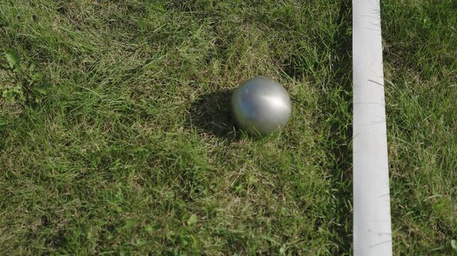A metal throwing ball falls on the lawn next to the markings