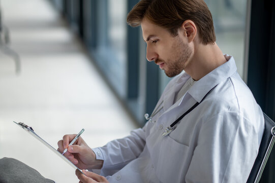 Young physician making medical records while sitting - Powered by Adobe