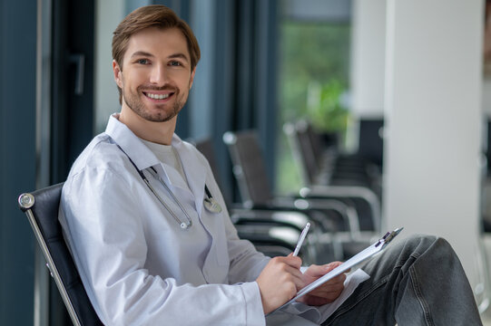 Male doctor writing notes on clipboard in clinic