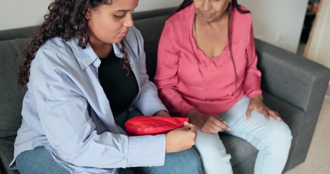 African daughter using first aid kit at home for her mother - Medicine, accident and family concept 