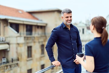 Professional Man And Woman Chatting On Balcony With City View In Casual Outdoor Office Conversation