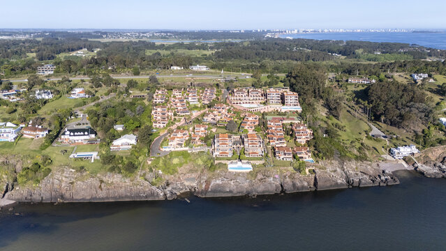 Aerial view of terracotta rooftops cascade down to meet the dark, shimmering waters, a coastal community bathed in the warm glow, Maldonado, Maldonado Department, Uruguay.