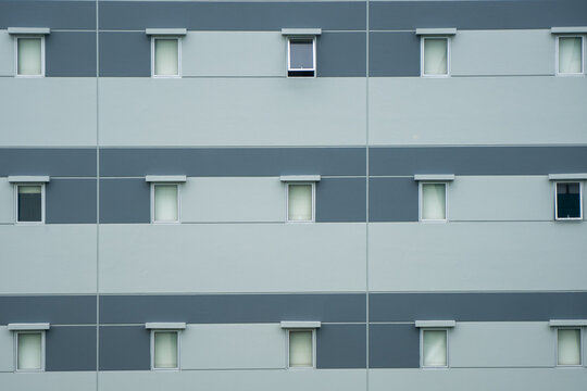 modern building facade, Uniform facade of a light gray and dark blue modern apartment or hotel building with multiple repetitive rectangular windows - Powered by Adobe