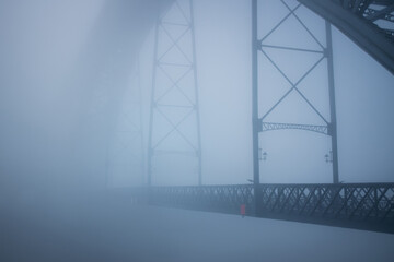 A dense fog envelops the Dom Lu&iacute;s I Bridge in Porto, Portugal, softening its steel structure into faint silhouettes. The scene feels quiet, surreal, and almost weightless.