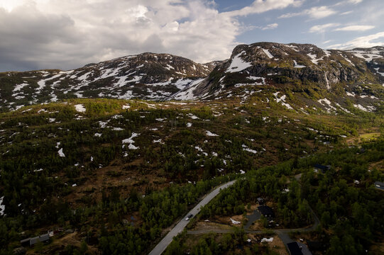 Aerial view of a winding road cutting through a landscape dotted with trees and patches of snow under a cloudy sky, Dalen, Telemark, Norway.